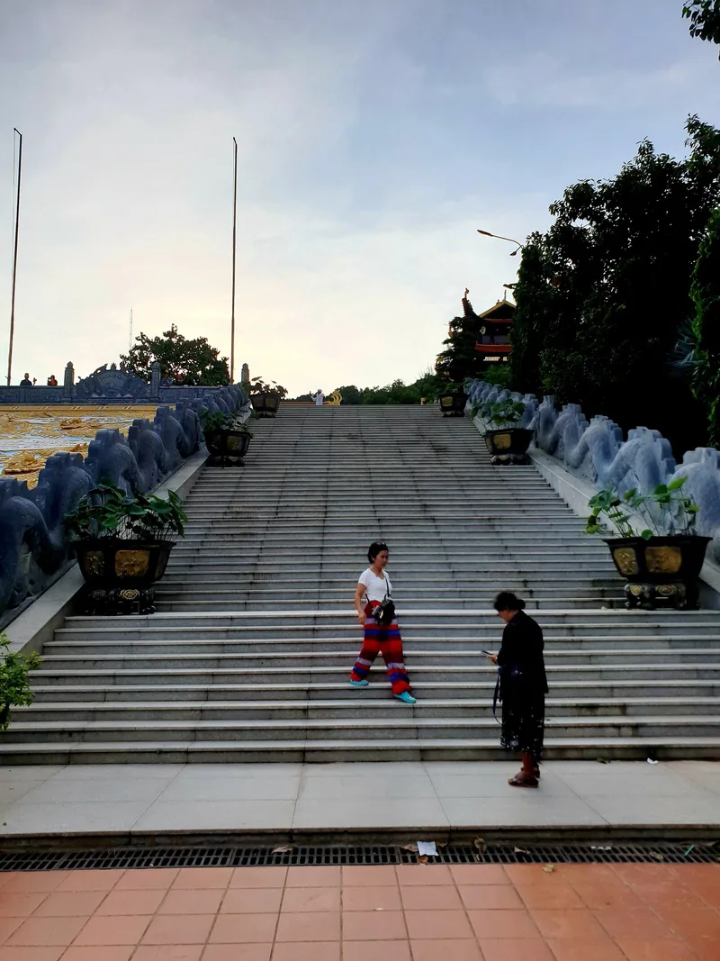 Du khách bước xuống bậc thang đá rộng của chùa Hộ Quốc ở Phú Quốc lúc hoàng hôn.