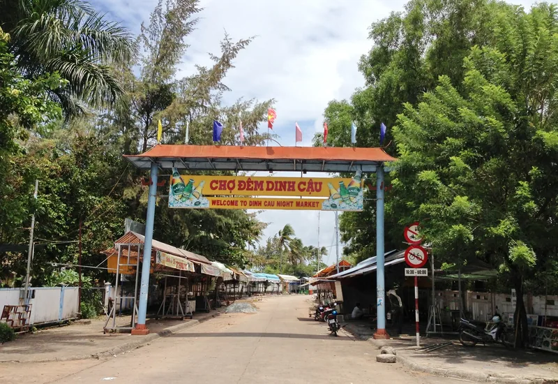 Cổng vào chợ đêm Dinh Cậu ở Dương Đông, Phú Quốc, với cờ màu sắc và các gian hàng còn đóng cửa vào ban ngày.