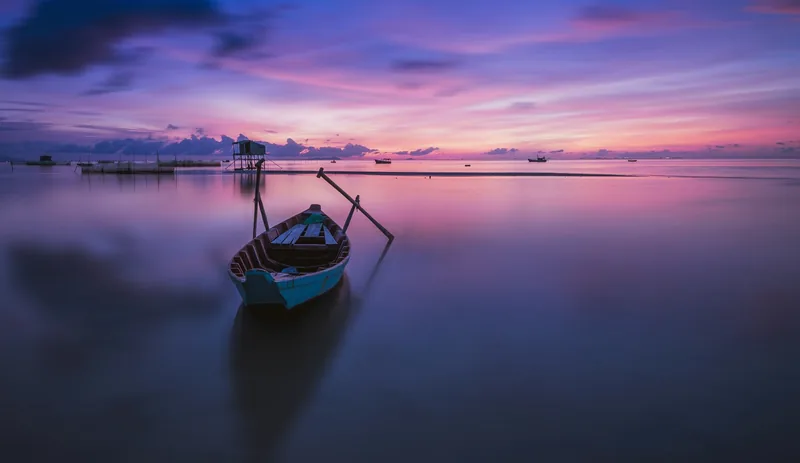Chiếc thuyền gỗ nhỏ neo trên mặt nước tĩnh lặng dưới bầu trời bình minh tím hồng rực rỡ ở Phú Quốc.