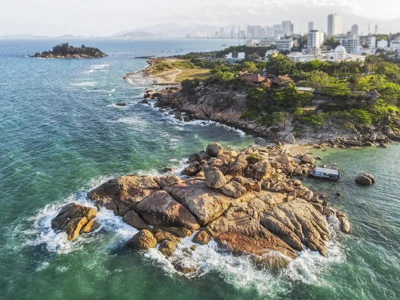 Toàn cảnh trên cao các tảng đá granite ven biển với đường chân trời thành phố phía sau tại Hòn Chồng